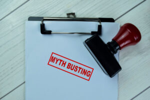A clip board with a white paper bearing a red ink stamp that says Myth Busting, used to accompany an excerpt from One Click Politics's white paper, Breaking Down the Walls of Advocacy and Nonprofits